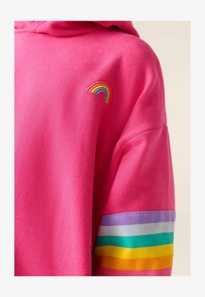 Vaaleanpunainen sweatshirt, jossa on pieni brodeerattu sateenkaari rinnassa ja sateenkaaren väreissä raidalliset nauhat yhdessä hihassa.