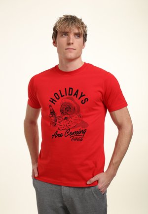 Red cotton t-shirt featuring a black graphic of Santa holding a Coke, text reading "Holidays Are Coming," crew neck, short sleeves.