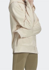 Ljusbeige hu hoodie med dragkedjefickor, mjuk textur, lös passform och ribbade muddar. Kombinerad med olivgröna leggings.