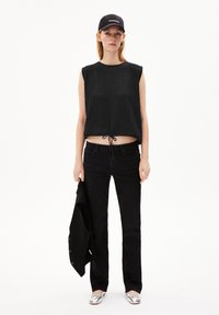 Black textured sleeveless top with tie at the waist, paired with black jeans and a black jacket, complemented by silver shoes and a cap.