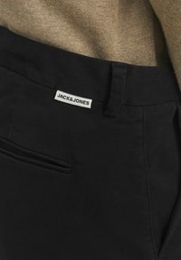 Crne hlače od pamuka s glatkom teksturom, s bočnim džepom i bijelom etiketom na pojasu s natpisom "JACK & JONES."