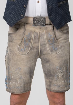Traditionelle beige Lederlederhosen mit blauen bestickten Mustern und einer detaillierten silbernen Gürtelschnalle, getragen zu einem weißen Hemd und einer dunklen Weste.