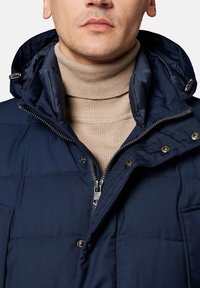 Granatowa ocieplana kurtka z odpinanym kapturem, zamkiem błyskawicznym i zatrzaskami. Posiada beżowy golf z prążkowanej dzianiny pod spodem.