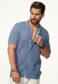 Hellblauer Strickcardigan mit lockerem, offenem Gewebe, kurzen Ärmeln und Knopfverschluss. Mit einem kontrastierenden, einfarbigen Kragen und Stickdetails.