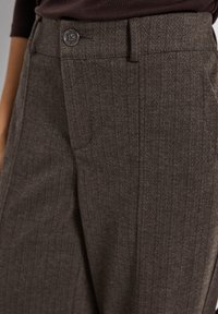 Bruna herringbone-byxor med en slät textur, med en knappstängning och en skräddarsydd passform som framhäver vertikala ränder.