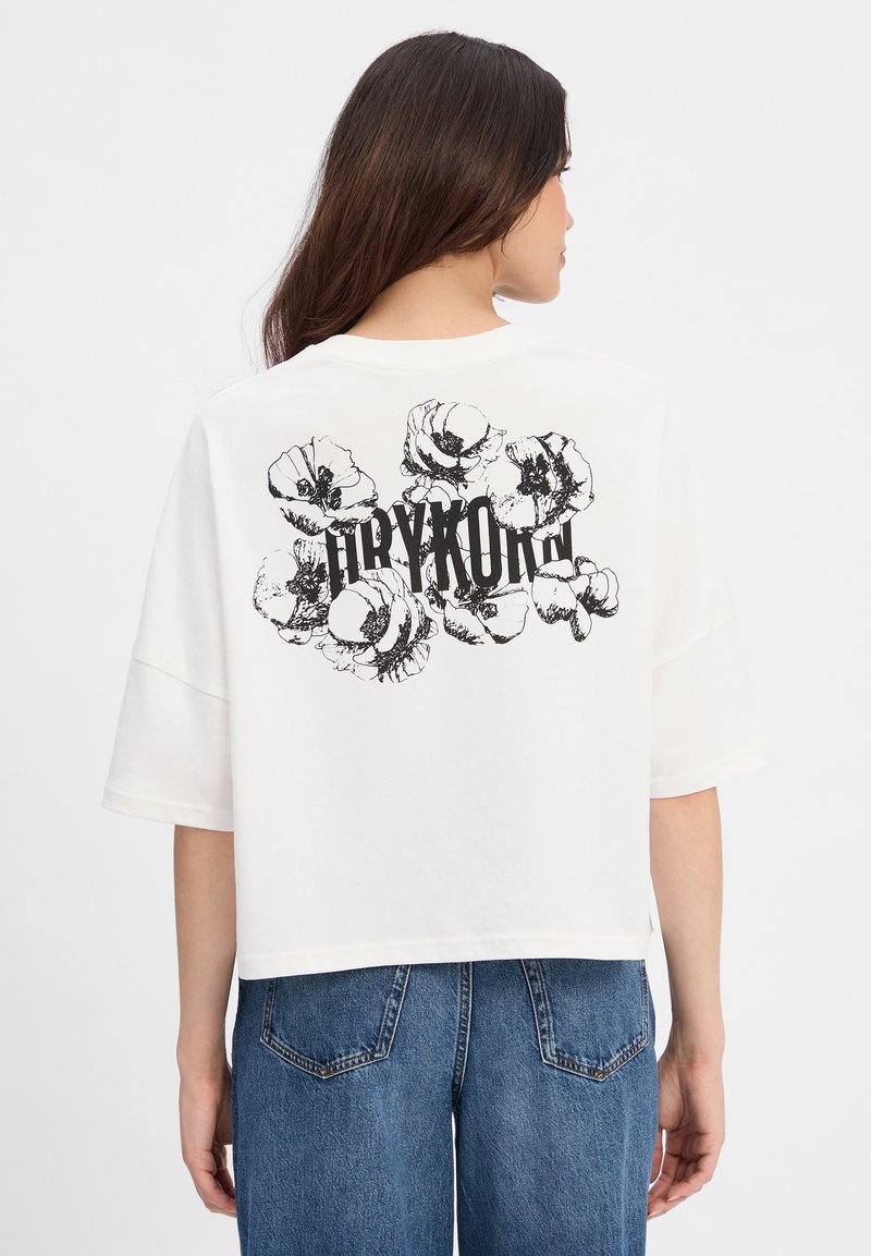 Weißes, kurzes T-Shirt mit einem schwarzen grafischen Design von Blumen und Text auf der Rückseite. Die Ärmel sind locker geschnitten und leicht oversized.