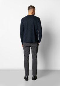 Marineblaues langärmliges Hemd mit einem strukturierten Design, kombiniert mit grauen Hosen. Schwarze Schuhe runden das Outfit ab. Ansicht von hinten.