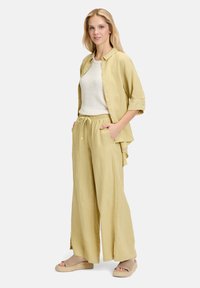 Linnen tweedelig outfit in zacht geel, bestaande uit een knoopshirt en wijdvallende broek met een elastische tailleband. Draag het met lichte, sleehakken.