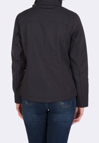 Czarna kurtka softshell z wysokim kołnierzem, dopasowanym krojem i widocznym szwem. Noszona z niebieskimi dżinsami, z niewielkim rozkloszowaniem u dołu.