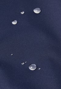 Des gouttes d'eau perlent sur un tissu bleu foncé déperlant, mettant en évidence la propriété hydrophobe du matériau.