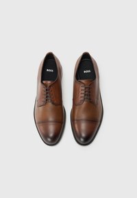 Scarpe in pelle marrone con finitura testurizzata, punte rotonde e design della punta liscia. Presentano una chiusura con lacci e solette con logo.