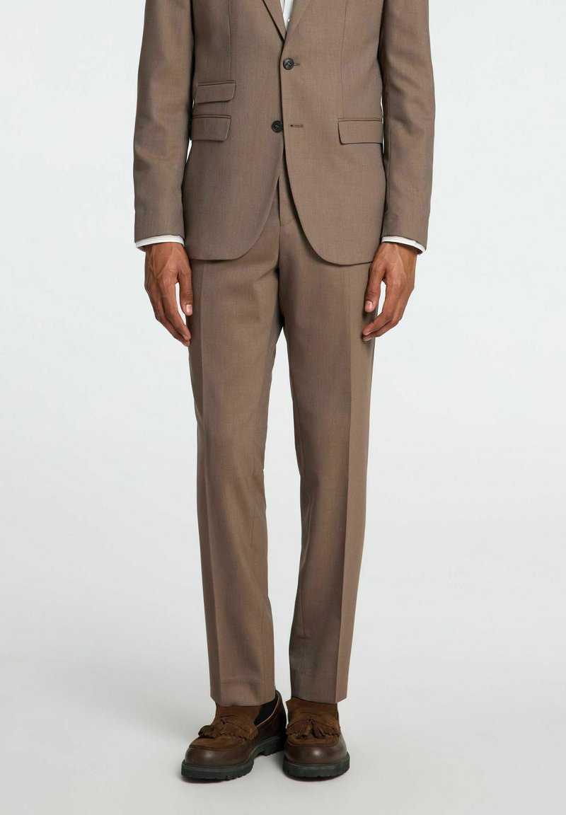 Bruin op maat gemaakt pak met een getailleerde blazer met twee zakken en een éénknops sluiting, gecombineerd met bruine gestructureerde schoenen.