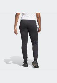Leggings ajustados negros hechos de una tela elástica, con una textura suave y una cintura elástica, usados con una camiseta blanca y zapatos negros.