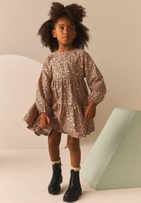 Braun gepunktetes Leopardmusterkleid mit langen Ärmeln und Rüsche am Saum, kombiniert mit schwarzen Knöchelstiefeln mit einem gerippten Strickdetail an der Oberkante.
