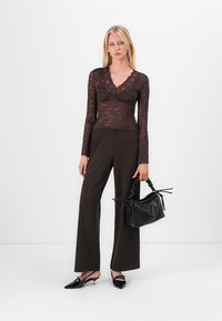 Svart blonder langermet bluse med v-hals, kombinert med mørkebrune vide bukser og en svart teksturert håndveske. Spisse svarte slingback hæler.