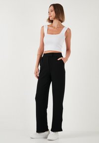 Zwarte hoge taillebroeken met een rechte snit, gecombineerd met een witte, strakke crop top. Glad materiaal met minimale details. Witte sneakers maken de look compleet.