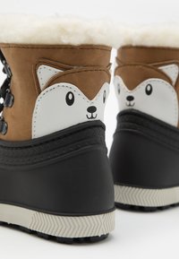 Bottes marron et blanches avec un motif de tête de renard, doublure en fourrure, semelle en caoutchouc noir et semelle extérieure blanche texturée.