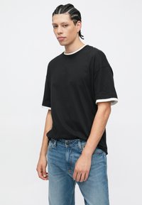 Μαύρο κοντομάνικο μπλουζάκι με λευκή επένδυση στον λαιμό και τα μανίκια, συνδυασμένο με ανοιχτόχρωμο τζιν παντελόνι. Απλός σχεδιασμός, βαμβακερό υλικό.