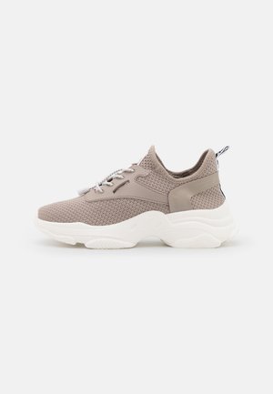 Lysebrun strikket stofsneaker med hvid chunky sål, snørelukning foran og trækstrop på hælen, set fra siden.