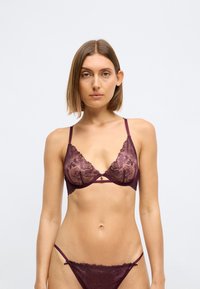 Bralette de encaje burdeos con patrón floral, straps ajustables y un pequeño colgante decorativo en el centro. Incluye un tanga de encaje a juego.