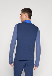 Long-sleeve athletic top in mixed blue shades, featuring a textured pattern, fitted design, and thumbholes on cuffs.