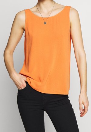Top sin mangas de color naranja brillante combinado con pantalones negros, complementado con un pequeño colgante redondo en el collar.