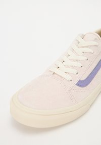 Baskets en daim rose clair avec lacets blancs, semelle en caoutchouc crème et une bande latérale violette sur fond blanc.