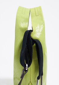 Zielona skórzana torba o błyszczącej fakturze, z dwiema płaskimi uchwytami i czarnym materiałowym paskiem. Minimalistyczny design z gładkim wykończeniem.