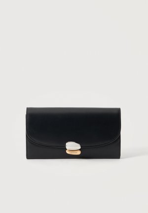 Portefeuille en cuir noir avec un rabat courbé et un fermoir argent et or gravé de "Calvin Klein" sur un fond uni.