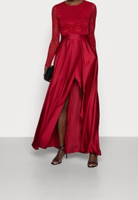 Abito rosso con top in pizzo a maniche lunghe e gonna in satin con un'alta alta. Abbinato a una clutch nera e sandali neri con cinturini.