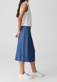 Vit ärmlös topp tillsammans med en blå denim midi-kjol med en smockad midja. Bärs med vita sneakers.