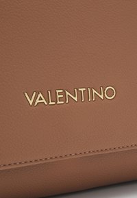 Borsa in pelle color cuoio con finitura testurizzata, caratterizzata dalla scritta dorata "VALENTINO" sul davanti. Linee pulite e design minimalista.