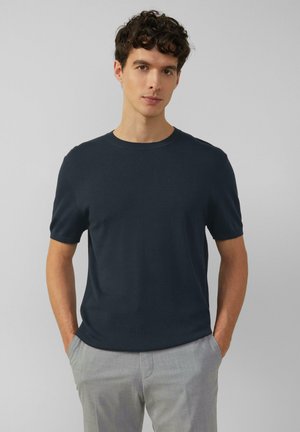 Navy short-sleeve t-shirt made of soft fabric, featuring a crew neckline and a relaxed fit, paired with light gray trousers.