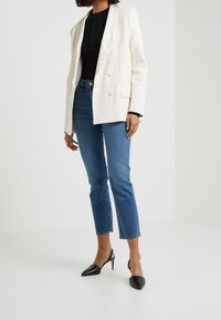 Vit dubbelknäppt kavaj med satinrevers, matchad med blå jeans i ankellängd och svarta spetsiga slingbackklackar.