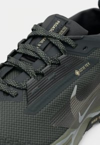 Tuvo plāns melniem un pelēkiem Nike Pegasus Trail 3 apaviem ar rakstainām šņorēm un Gore-Tex etiķeti sānos.