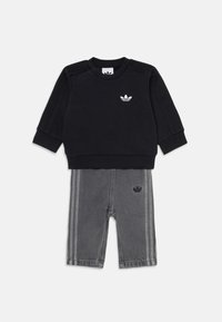 Sweatshirt noir avec des accents texturés aux épaules et un logo blanc, associé à un jogger en denim gris avec des rayures verticales sur les côtés et un détail de logo.