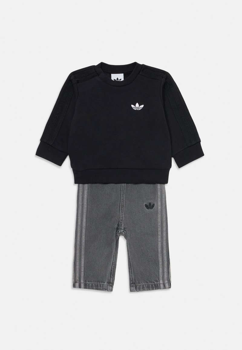 Juodas džemperis su tekstūruotais pečių akcentais ir balta logotipu, derinamas su pilkais džinsų tipo tregais su vertikaliomis šoninėmis juostomis ir logotipo detale.