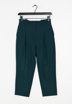 Pantaloni a vita alta color turchese con pieghe, caratterizzati da una texture liscia e una lunghezza cropped, appesi a un gancio nero.
