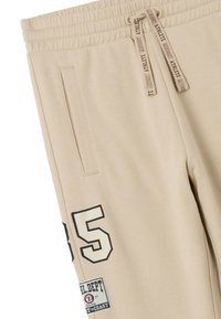 Beige joggerbroeken met een elastische tailleband, trekkoord, zijzakken en een groot "85" graphic met een patchdetail op het been.