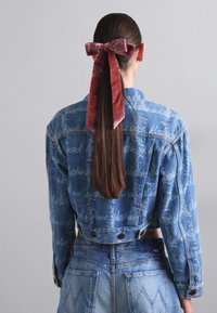 Izgriezts džinsu jaka ar zilu mazgāšanu, kurai ir balti teksta raksti un pogu akcenti. Sarkans samta arcs matos noslēdz izskatu.