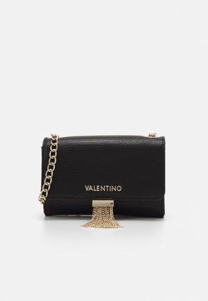 Bolso de mano de cuero negro con textura de cocodrilo, herrajes dorados, correa de cadena y un detalle de borla en la parte delantera. Logo de la marca mostrado de manera prominente.