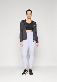 Čierny športový crop top, šedá mikina s kapucňou, svetlofialové legíny a čierne tenisky s bielymi akcentmi. Hladké textúry, priliehavý dizajn.