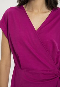 Fuksia wrap mekko lyhyillä hihoilla, jossa on V-mallinen kaula-aukko ja sidottu vyötärödetaali, valmistettu pehmeästä, tekstuurista kankasta.