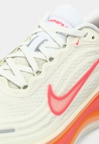 Αθλητικό παπούτσι Nike για τρέξιμο με λευκό υφασμάτινο επάνω μέρος, που διαθέτει ροζ διαφανές λογότυπο και πολύχρωμη μεταβαλλόμενη σόλα σε αποχρώσεις πορτοκαλί και ροδάκινου.