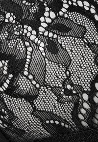 Tissu en dentelle noire avec des motifs floraux, une texture en maille fine, et des niveaux d'opacité variables avec des détails complexes et des bords festonnés.