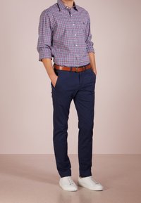 Rutig skjorta med knappar i blått, rosa och vitt, kombinerad med marinblå chinos och vita sneakers. Ett brunt läderbälte accentuerar outfiten.