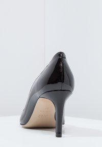 Černá lakovaná vysoká botka z pohledu zezadu, s špičatou špičkou a štíhlým podpatkem na bílém pozadí.