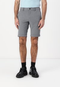 Grå strikkede shorts med rullekanter, med en enkelt knappelukking og beltehemper. Brukt med svarte lærsko og sokker.