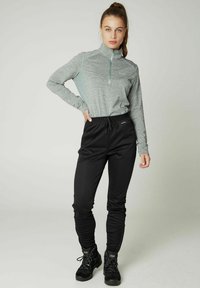 Lichtgrijze long-sleeve top met een halve rits en contrasterende mintaccenten, gecombineerd met zwarte elastische broek en zwarte laarzen.