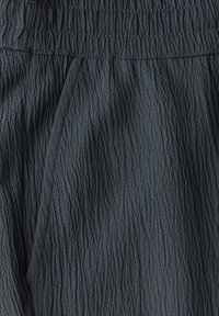 Tissu gris foncé, texturé avec un motif froncé. Taille élastique avec une finition lisse. Matériau léger et fluide.